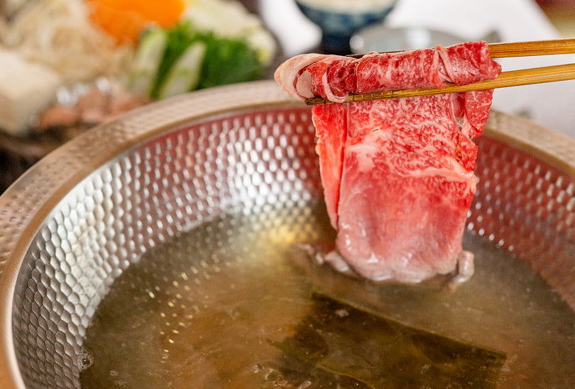 鍋の出汁に霜降り牛肉をしゃぶしゃぶする瞬間を捉えた、和牛料理の調理シーン