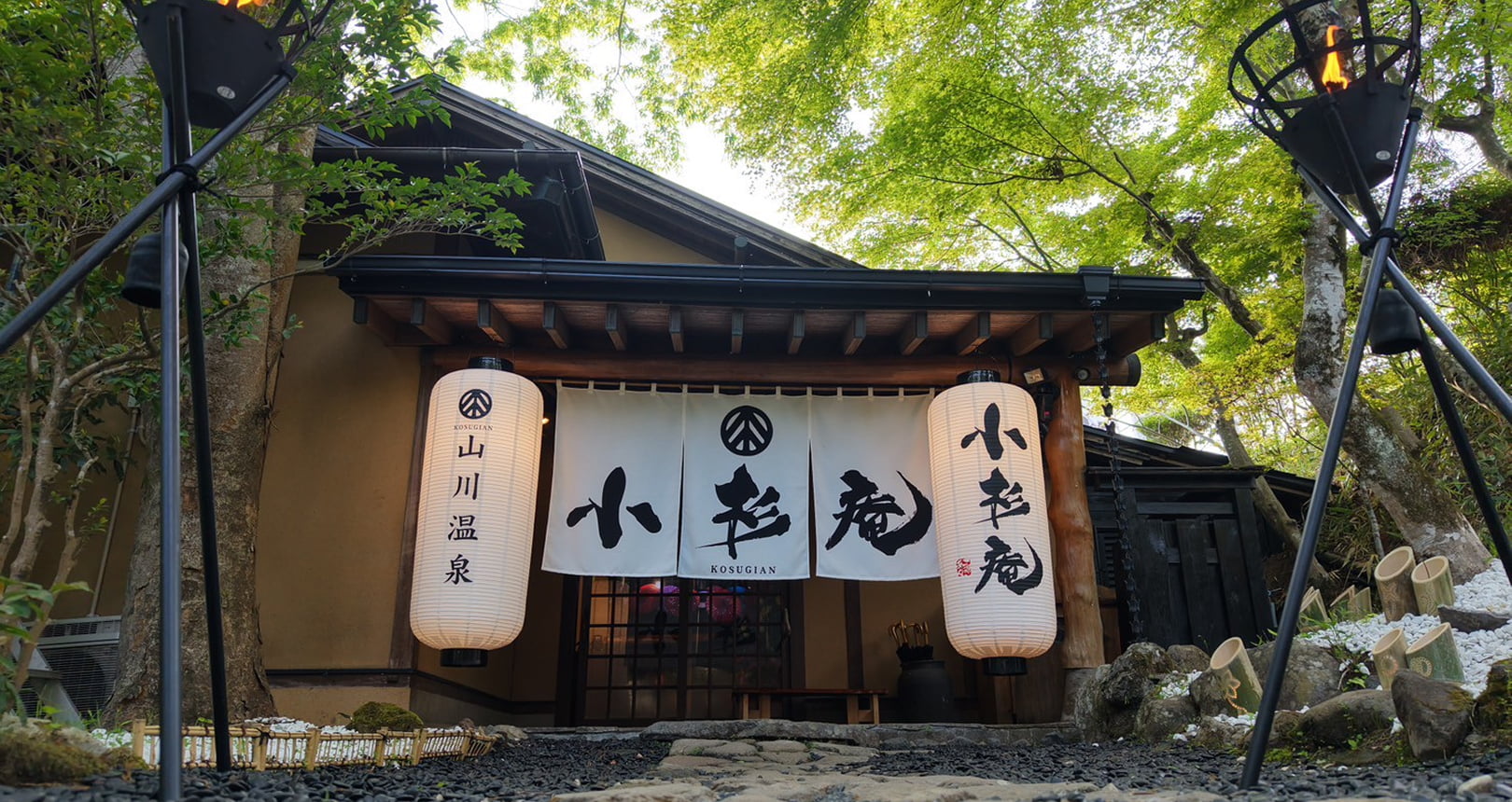 旅館の入口に吊るされた提灯と暖簾があり、「小杉庵」と書かれている山間の温泉宿の外観