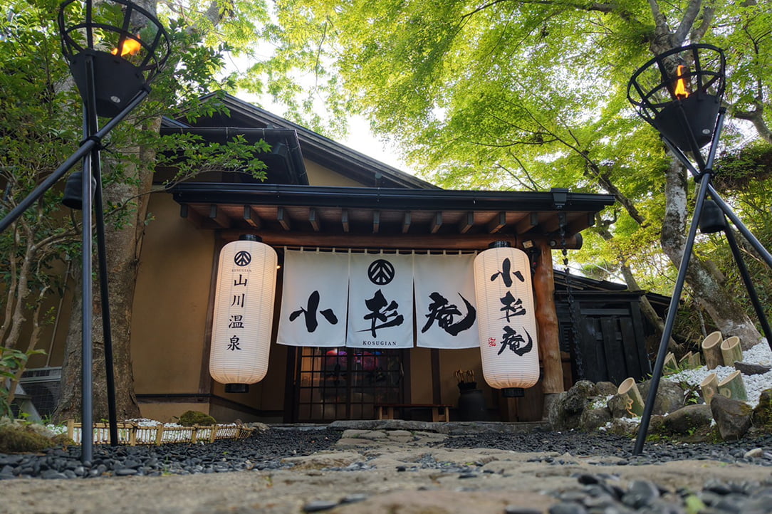 旅館の入口に吊るされた提灯と暖簾があり、「小杉庵」と書かれている山間の温泉宿の外観