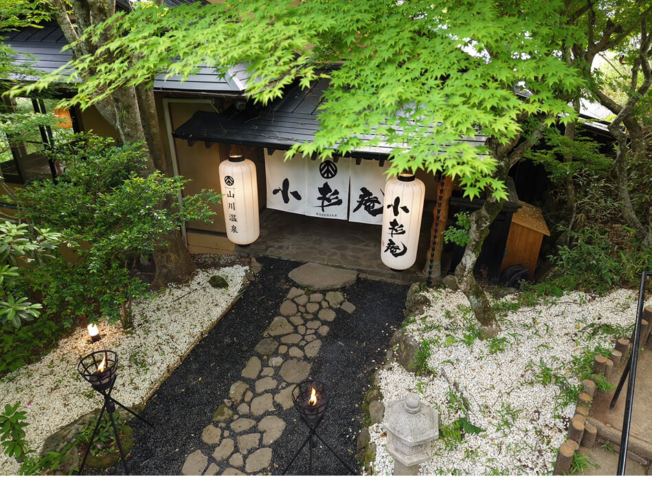 石畳の道と竹灯りが静かに迎える、緑に囲まれた和風建築の玄関前の風景